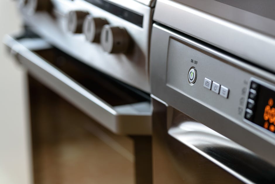 A person wearing a black shirt is placing a tray of cooked rice into a modern stainless steel oven with a digital display and control knobs. The oven's interior is illuminated, showing clean glass and metal surfaces. The surrounding kitchen wall is painted dark grey, and the oven is built into a cabinet. The individual is kneeling or sitting on the floor, focusing on surface cleaning or food placement, demonstrating domestic oven use and maintenance. The scene highlights the cleanliness and functional state of the oven, typical of professional cleaning services provided by Oven Cleaning Merton.